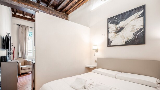 A hotel room with a bed, a desk, a chair, and a window with curtains. - Lambertesca Mono (Florence)