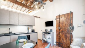 A compact kitchen with modern appliances, a dining area with a table and chairs, and a large wooden door. - Lambertesca Mono (Florence)