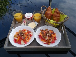 Una bandeja con dos tazones de ensalada de frutas, dos vasos de jugo de naranja, una cesta de cruasanes y un recipiente de mantequilla.