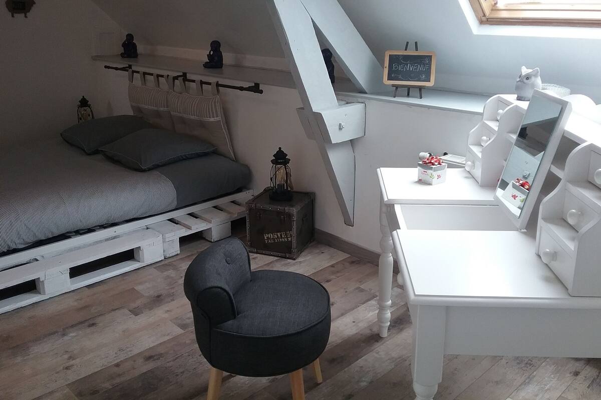 A bedroom with a loft bed, a desk with a computer, a chair, a small cabinet, and a skylight.