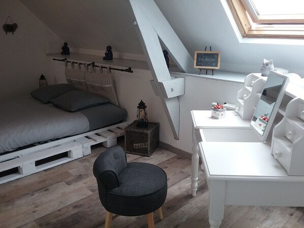 Un dormitorio con cama entrepiso, escritorio con computadora, silla, un mueble pequeño y tragaluz.