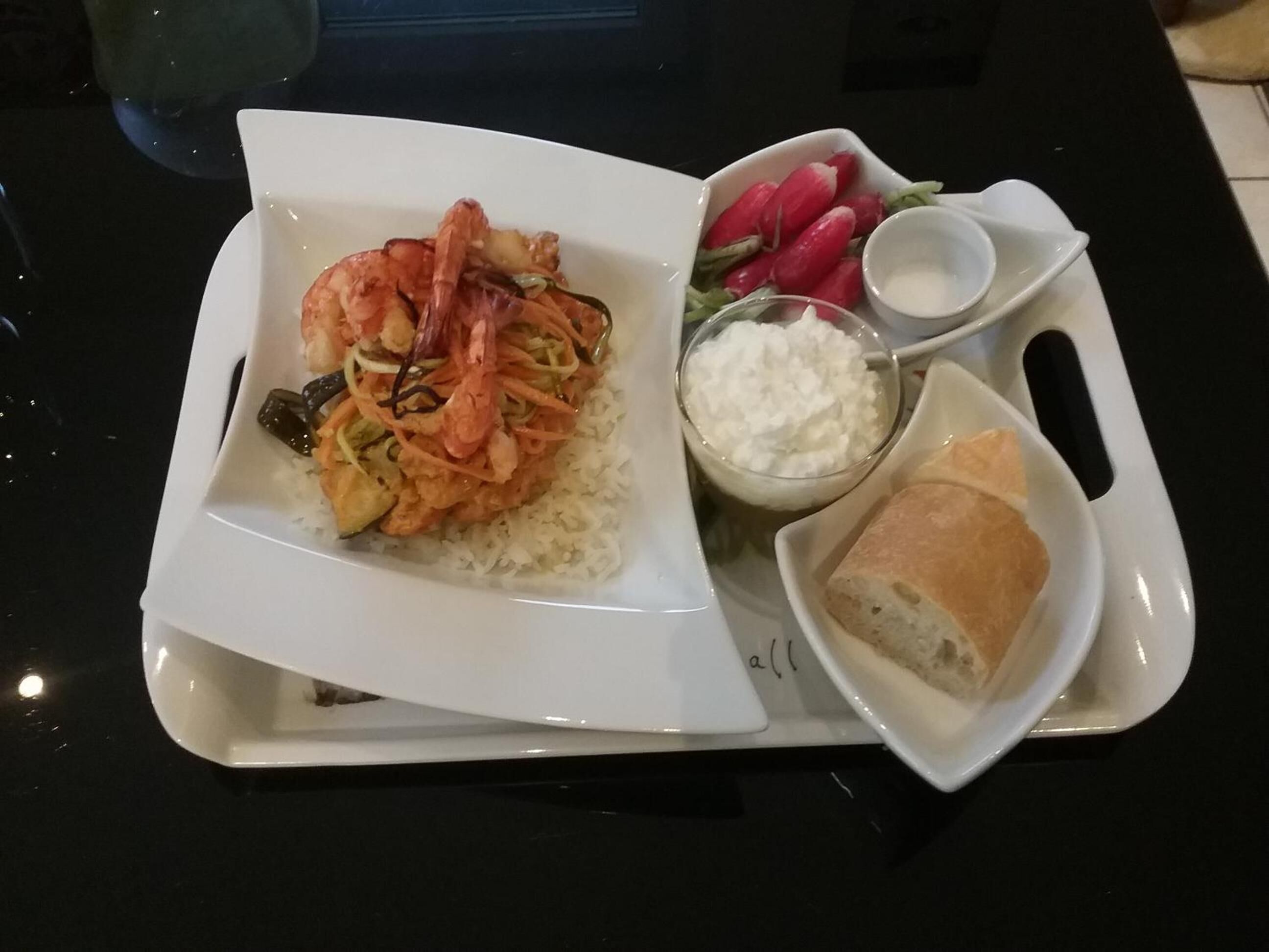 A tray with a plate of shrimp and rice, a bowl of radishes, a small bowl of sour cream, and a piece of bread.