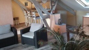 A cozy room with a high ceiling, exposed beams, a wicker chair, a small table with a lantern, and a peacock feather decoration. - Chambre d'hôtes Coquelicot (Nurlu)