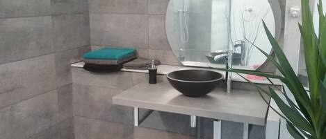 A bathroom with a round mirror, a black bowl sink, a green towel, and a plant.