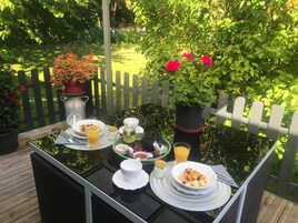 Mesa al aire libre con alimentos para el desayuno, rodeada de follaje y una cerca de madera.
