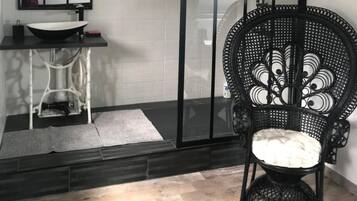 Un baño moderno con cabina de ducha de marco negro, lavabo blanco y silla de mimbre.