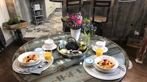 A breakfast table with two bowls of fruit, two cups of orange juice, a teapot, and a vase with flowers. - Chambre d'hôtes Coquelicot (Nurlu)