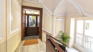 A hallway with a wooden door, a doormat, a marble floor, a potted plant, and a balcony with a wrought iron railing. - Be Italian Flat Duomo 319 (Naples)