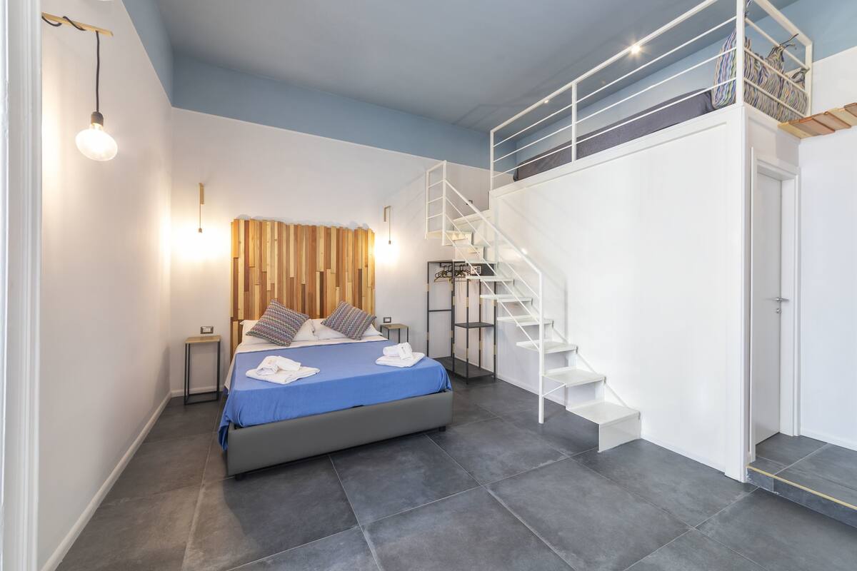 A modern bedroom with a bed, a wooden slat wall, a white staircase, and a small bedside table.