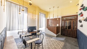 A hotel lobby with a reception desk, seating area with tables and chairs, and a shoe display wall. - Be Italian Flat Duomo 319 (Naples)