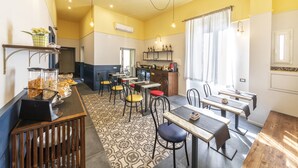 A dining area with tables and chairs, a buffet with food items, and a kitchen area with shelves and appliances. - Be Italian Flat Duomo 319 (Naples)