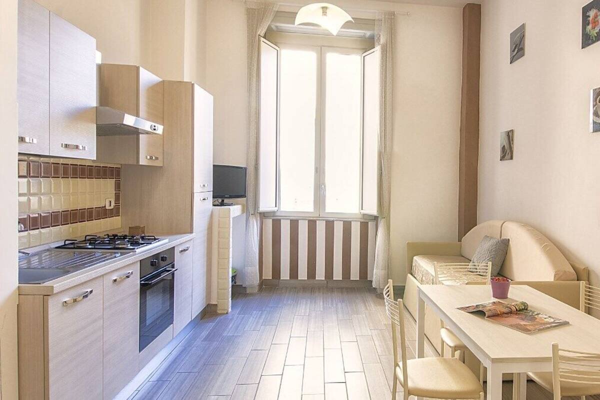A compact kitchen with a dining area, a window with curtains, and a flat-screen TV.