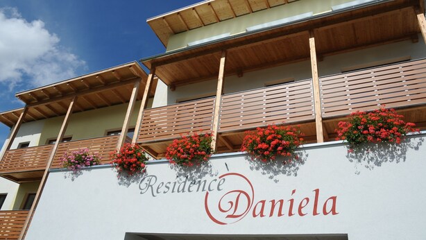 Un immeuble doté de balcons ornés de fleurs rouges et d’une enseigne indiquant « Résidence Daniela ».