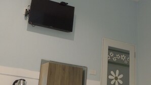 Una habitación con una cama, un escritorio, una silla, un televisor montado en la pared y una puerta con un diseño floral.