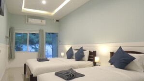 Habitación de hotel con dos camas, cada una con almohada y manta, una ventana con cortinas, un equipo de aire acondicionado y una lámpara de noche.