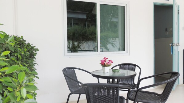 Un pequeño espacio al aire libre con una mesa redonda y cuatro sillas, una planta en maceta y una ventana con vistas a vegetación.