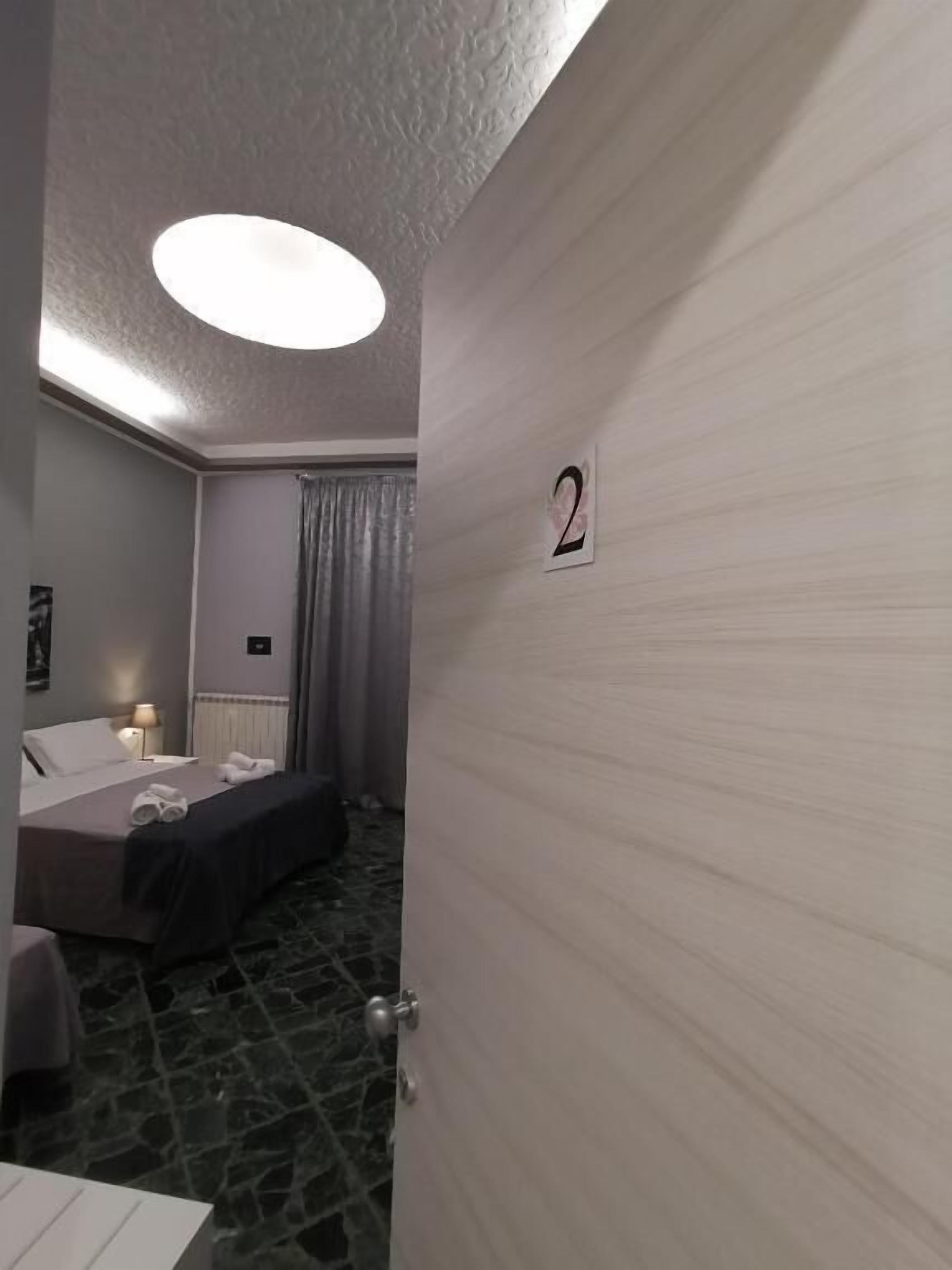 Habitación de hotel con cama, mesita de noche, lámpara y el número 2 en la pared.