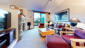 A living room with a stone wall, a television, a sofa, a coffee table, and a large window.