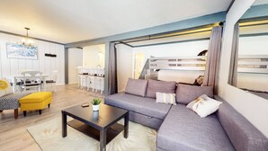 A modern living room with a grey sofa, yellow ottoman, and a black coffee table. There is a dining area with white chairs and a table in the background. - Mammoth Ski & Racquet Club #4 1 Bedroom Condo by RedAwning (Mammoth Lakes)