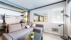 A modern living room with a grey sofa, a small coffee table with a plant, a bunk bed with a ladder, and a large mirror on the wall. - Mammoth Ski & Racquet Club #4 1 Bedroom Condo by RedAwning (Mammoth Lakes)