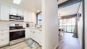 A modern kitchen with white cabinets, stainless steel appliances, and a dining area with a table and chairs. - Mammoth Ski & Racquet Club #4 1 Bedroom Condo by RedAwning (Mammoth Lakes)