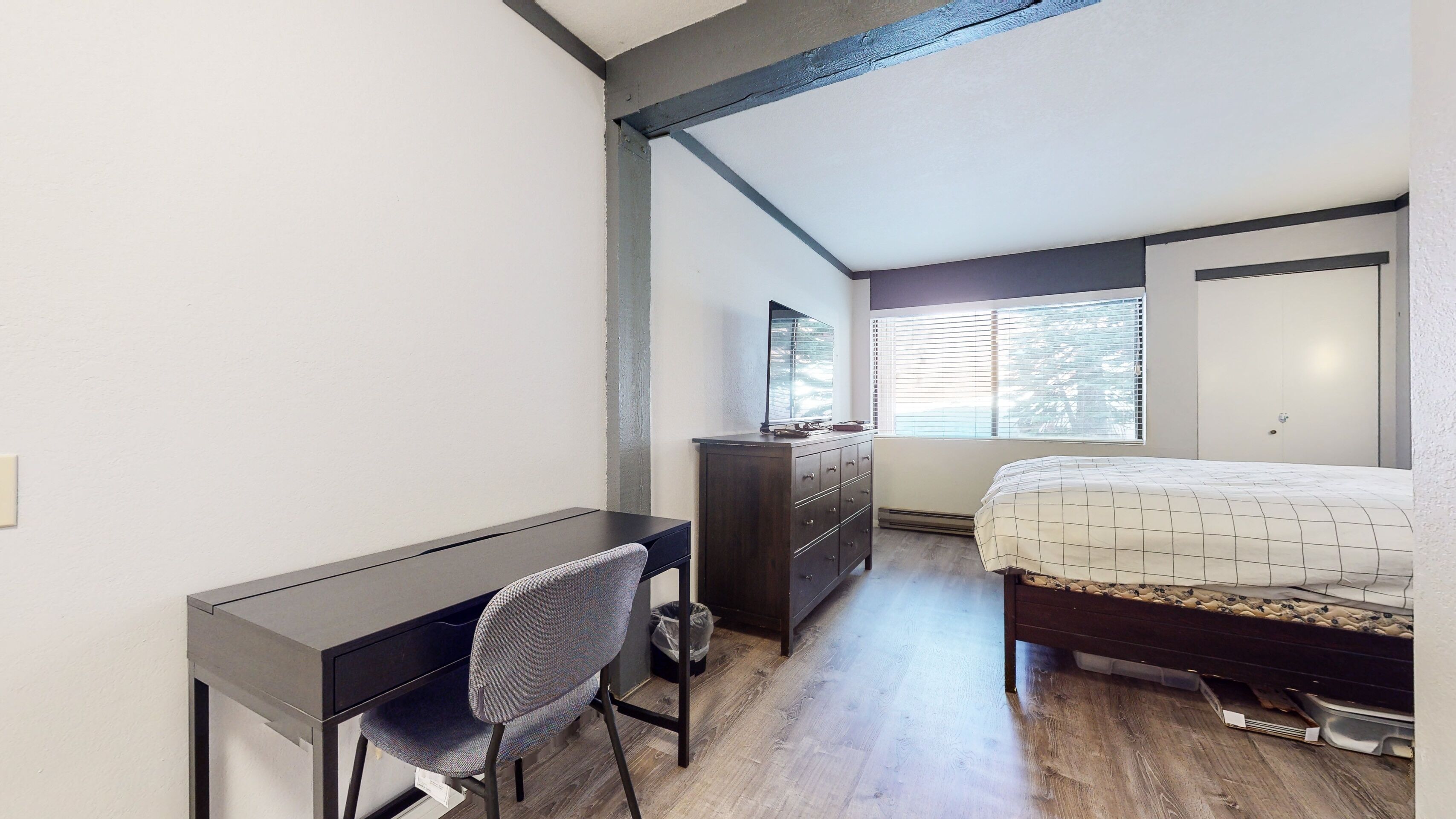 A bedroom with a bed, a desk, and a dresser.