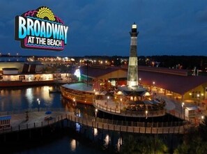 A waterfront area with a prominent lighthouse, a large illuminated sign reading "Broadway at the Beach," and a dock with boats. - Sea Cloisters 302b 2 Bedroom Condo by RedAwning (North Myrtle Beach)