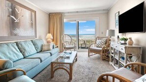 Una habitación de hotel con balcón, sofá, sillón, mesa de centro y televisor.