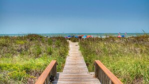 A wooden boardwalk leading to a beach with colorful umbrellas and flags. - Sea Cloisters 303e 2 Bedroom Condo by RedAwning (North Myrtle Beach)