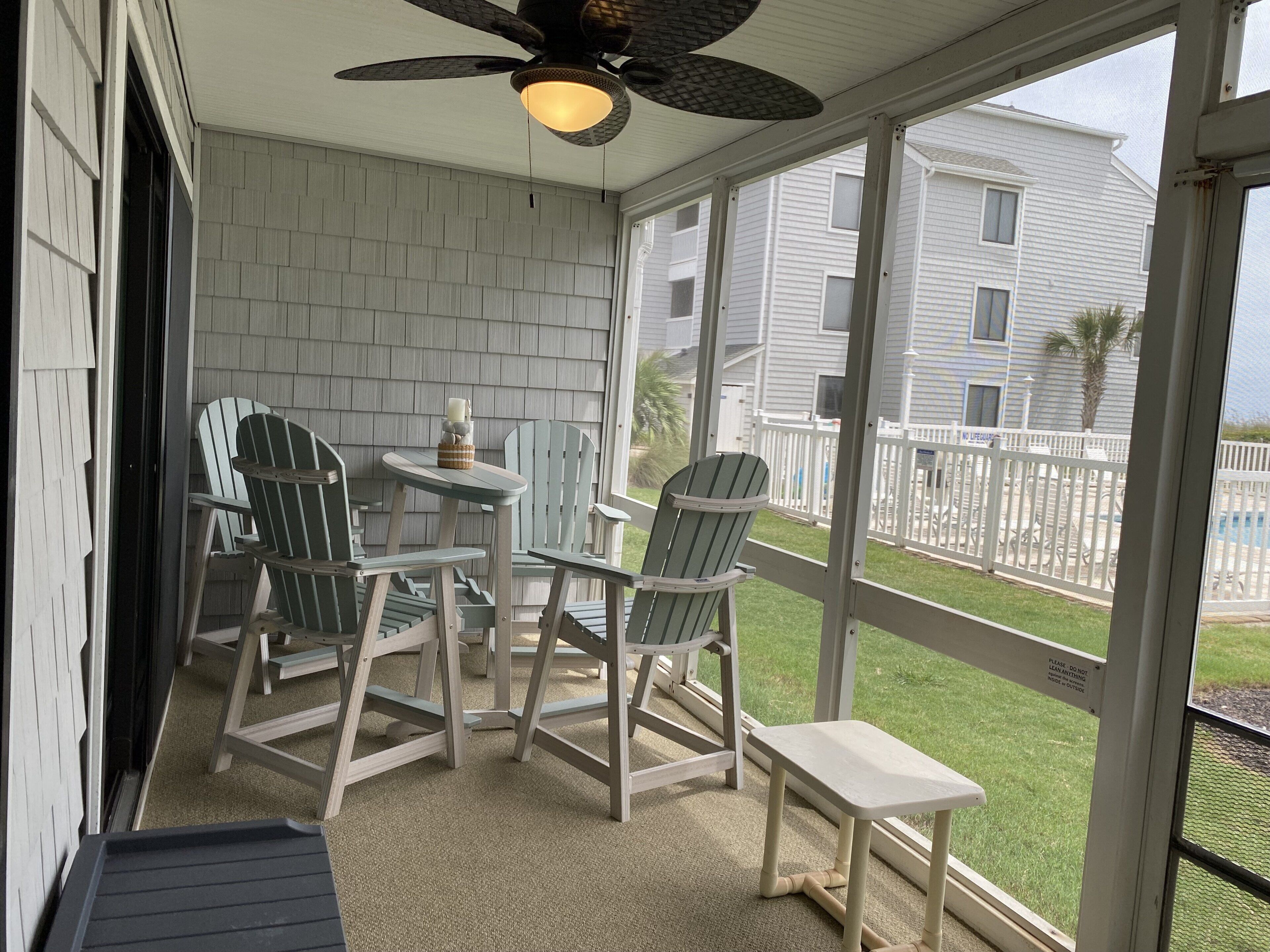 A covered outdoor seating area with Adirondack chairs and a small table, overlooking a residential neighborhood.