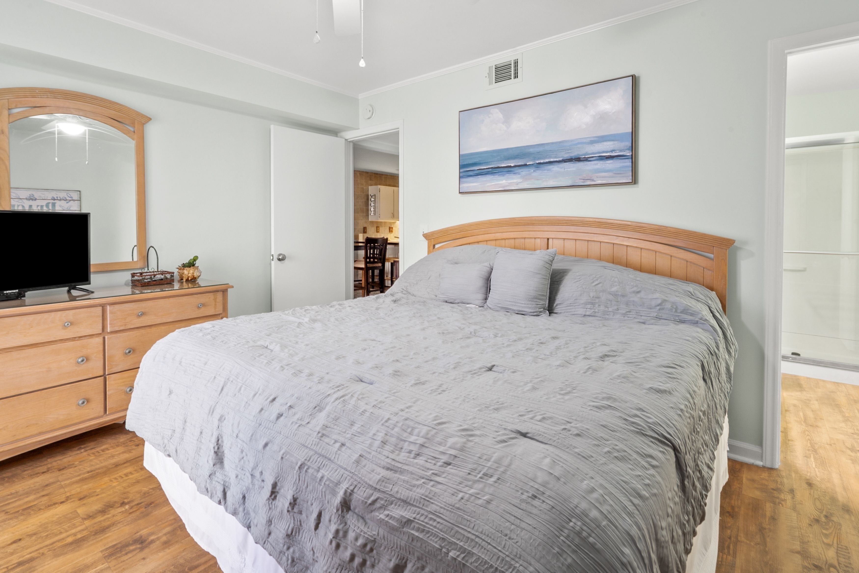 Ein Schlafzimmer mit einem großen Bett, einem Schminktisch, einem Fernseher und einem Bild vom Meer.