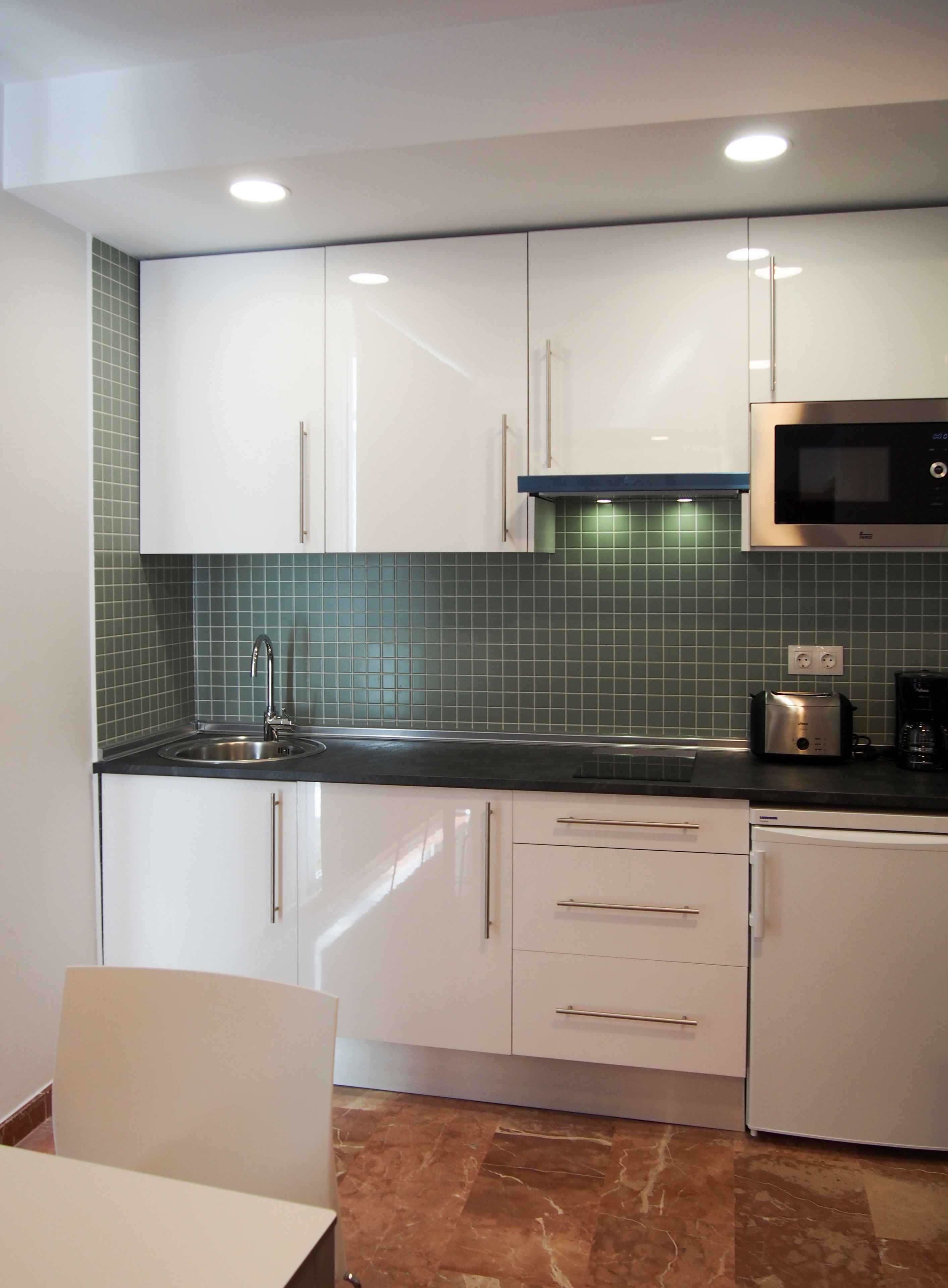 Una cocina moderna con gabinetes blancos, un lavamanos de acero inoxidable, un microondas y un tostador.