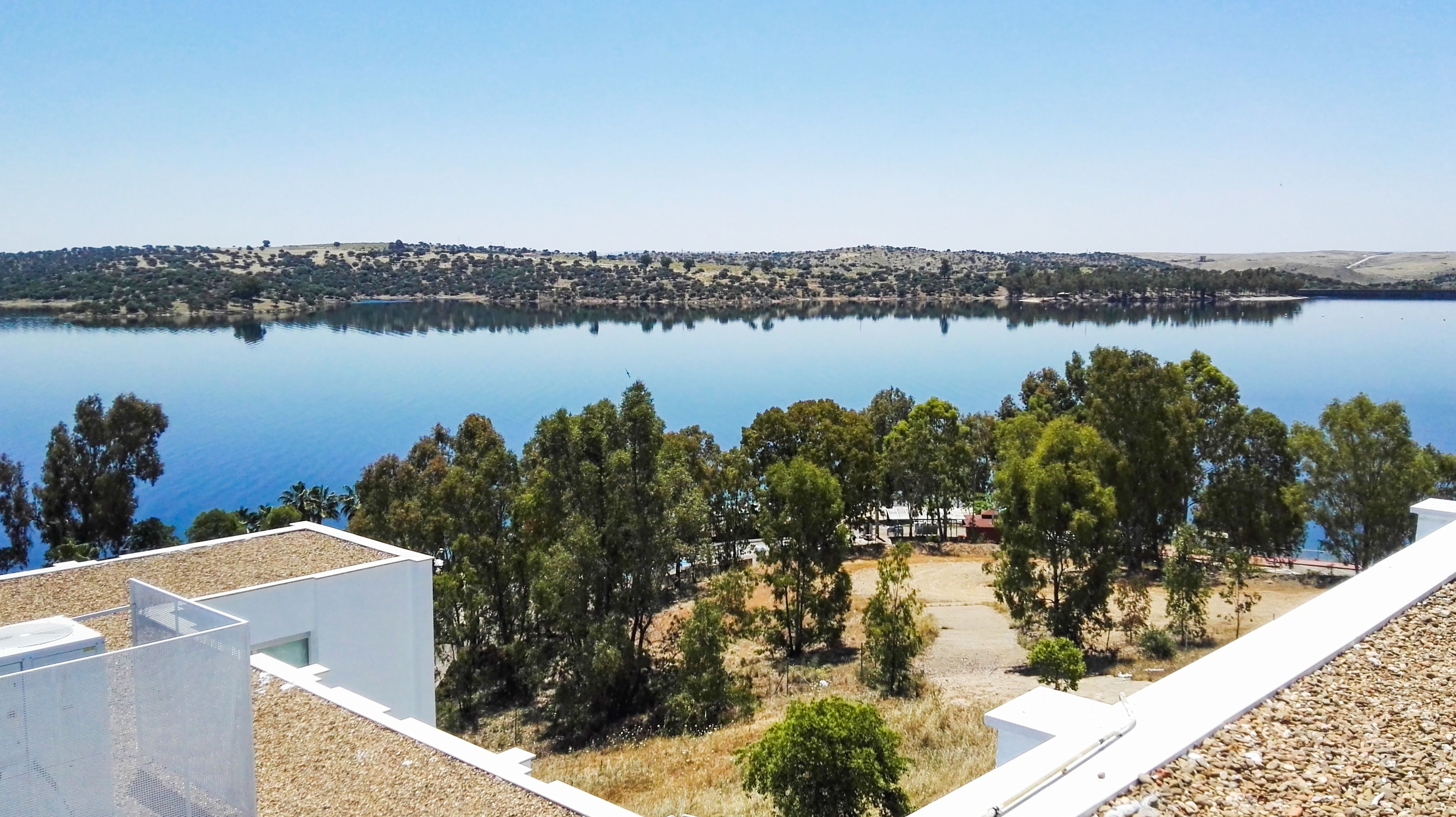 Vista a orillas de un lago con cielo despejado, aguas tranquilas y un pueblo distante.