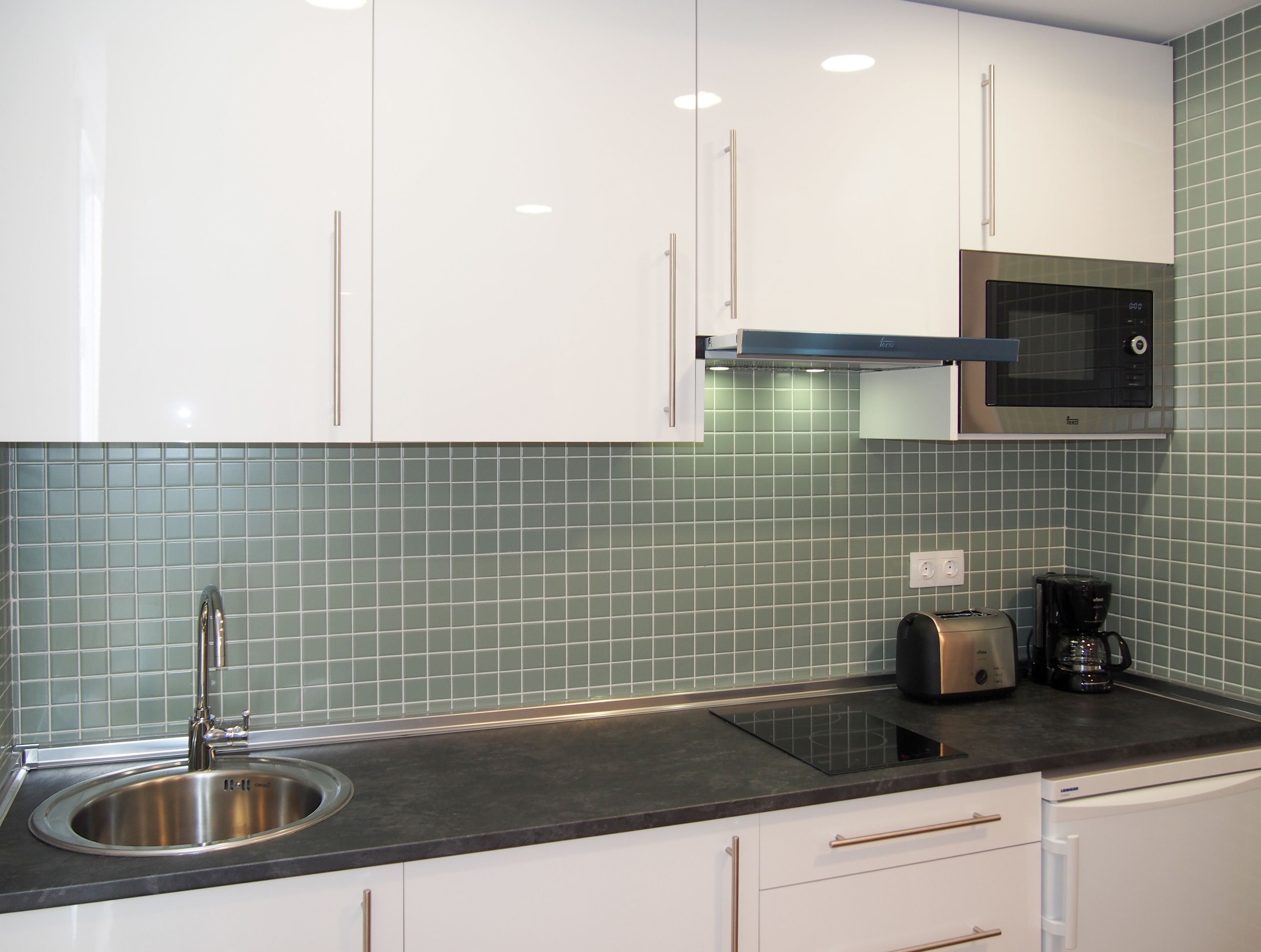A modern kitchen with white cabinets, a stainless steel sink, a black countertop, and a microwave.