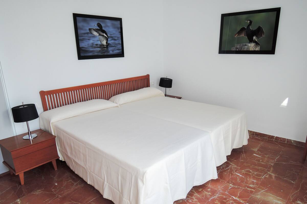A neatly made bed with a wooden headboard, a bedside table with a lamp, and two framed pictures on the wall.