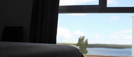 A room with a large window offering a view of a lake and distant hills.