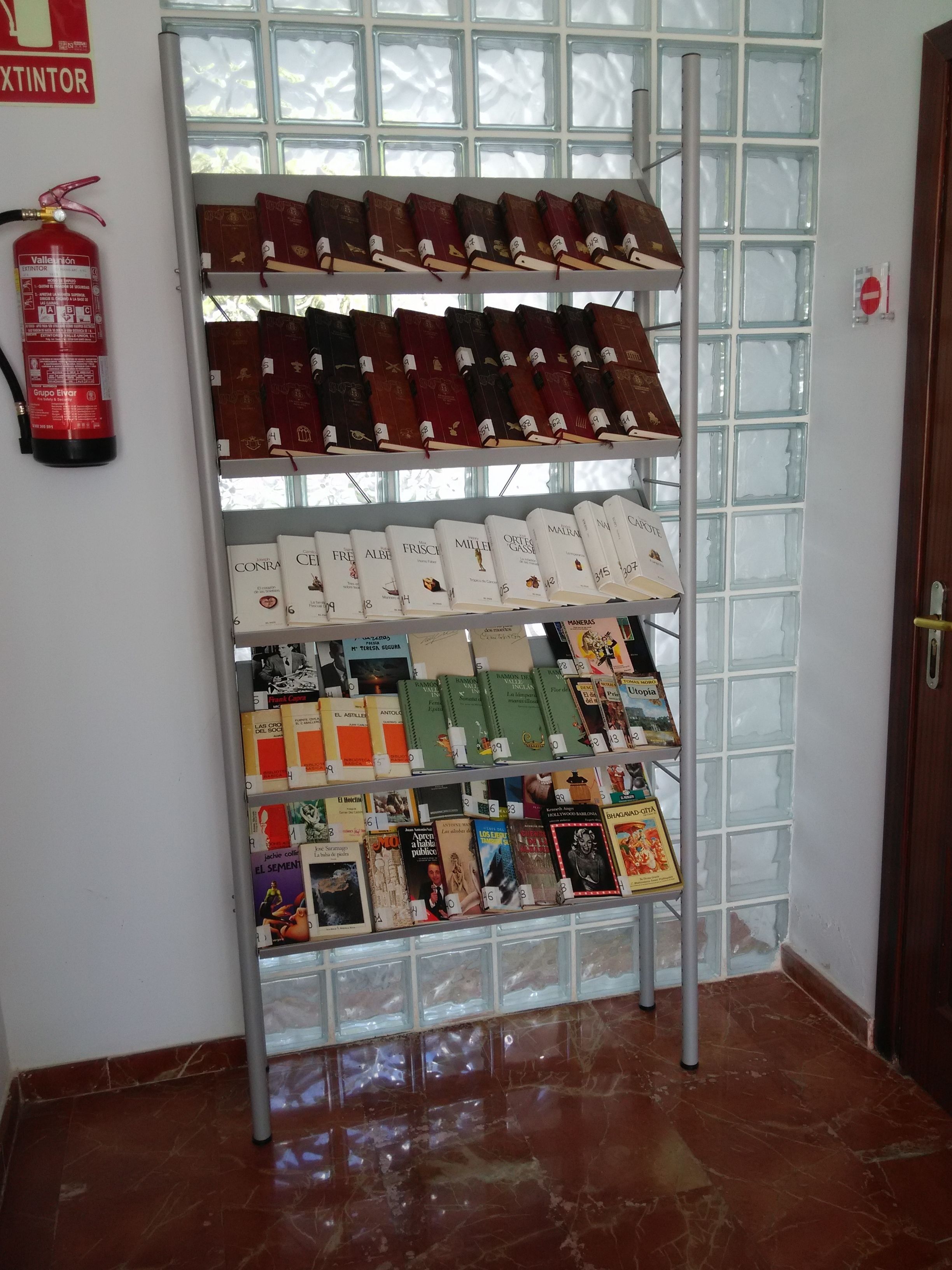 A book display rack in a room with a fire extinguisher on the wall and a tiled floor.