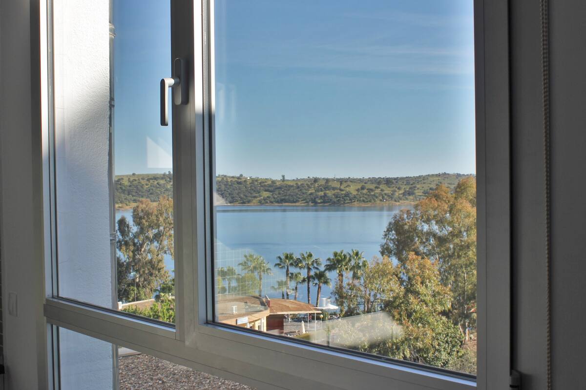 A view through a window of a lake with surrounding trees and a distant shoreline.