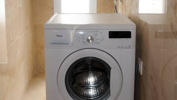 A front-loading washing machine in a bathroom with marble walls and a window.