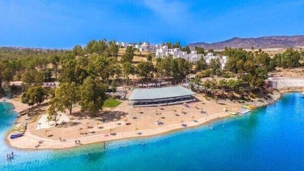 An aerial view of a coastal resort with a beach, a large building, and a mountainous backdrop. - Apartamentos Embalse de Orellana (Orellana la Vieja)