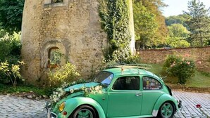 A vintage green car parked in front of a stone tower with ivy.