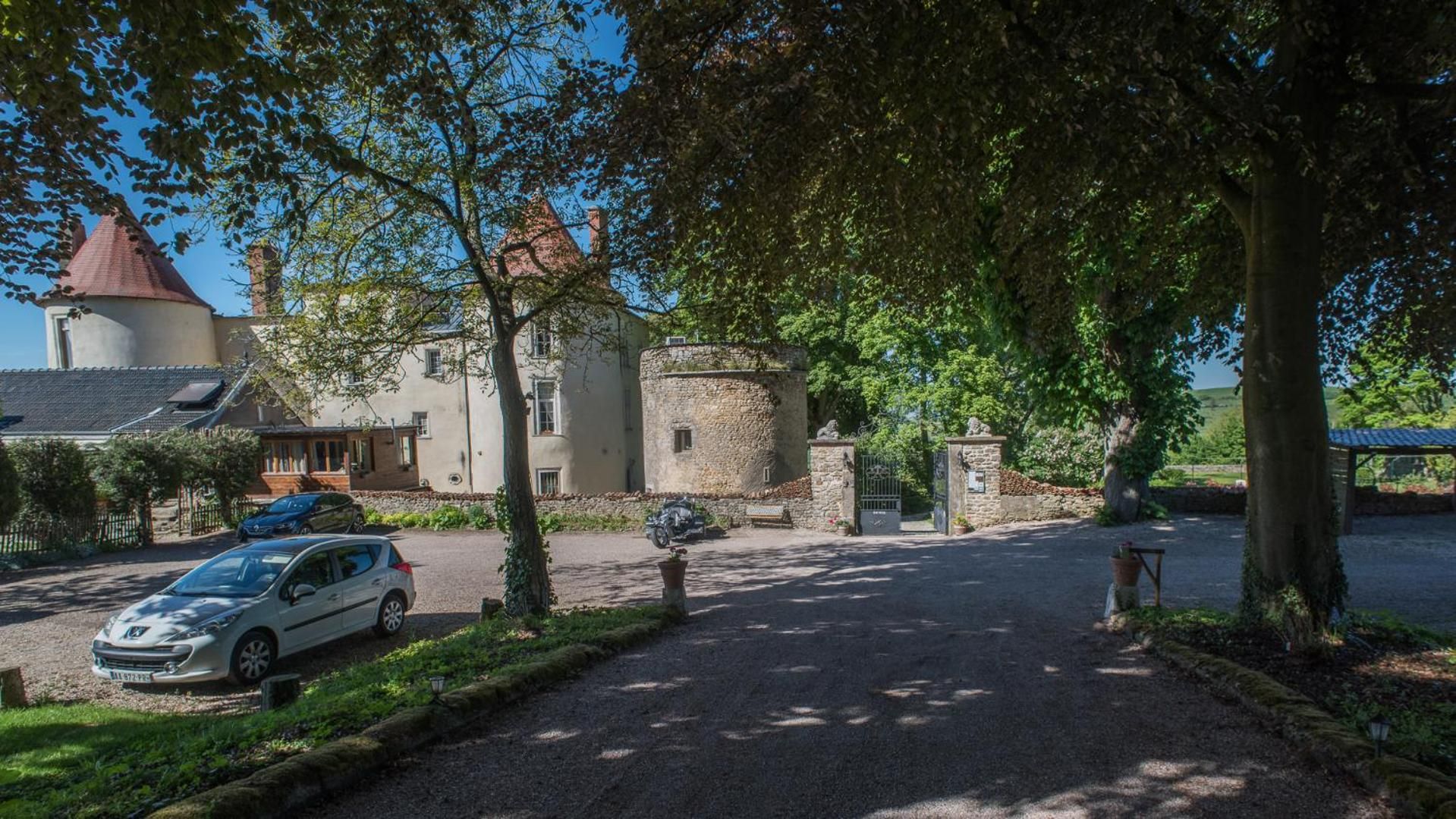 A paved driveway leading to a stone building with a tower, parked cars, and lush greenery.