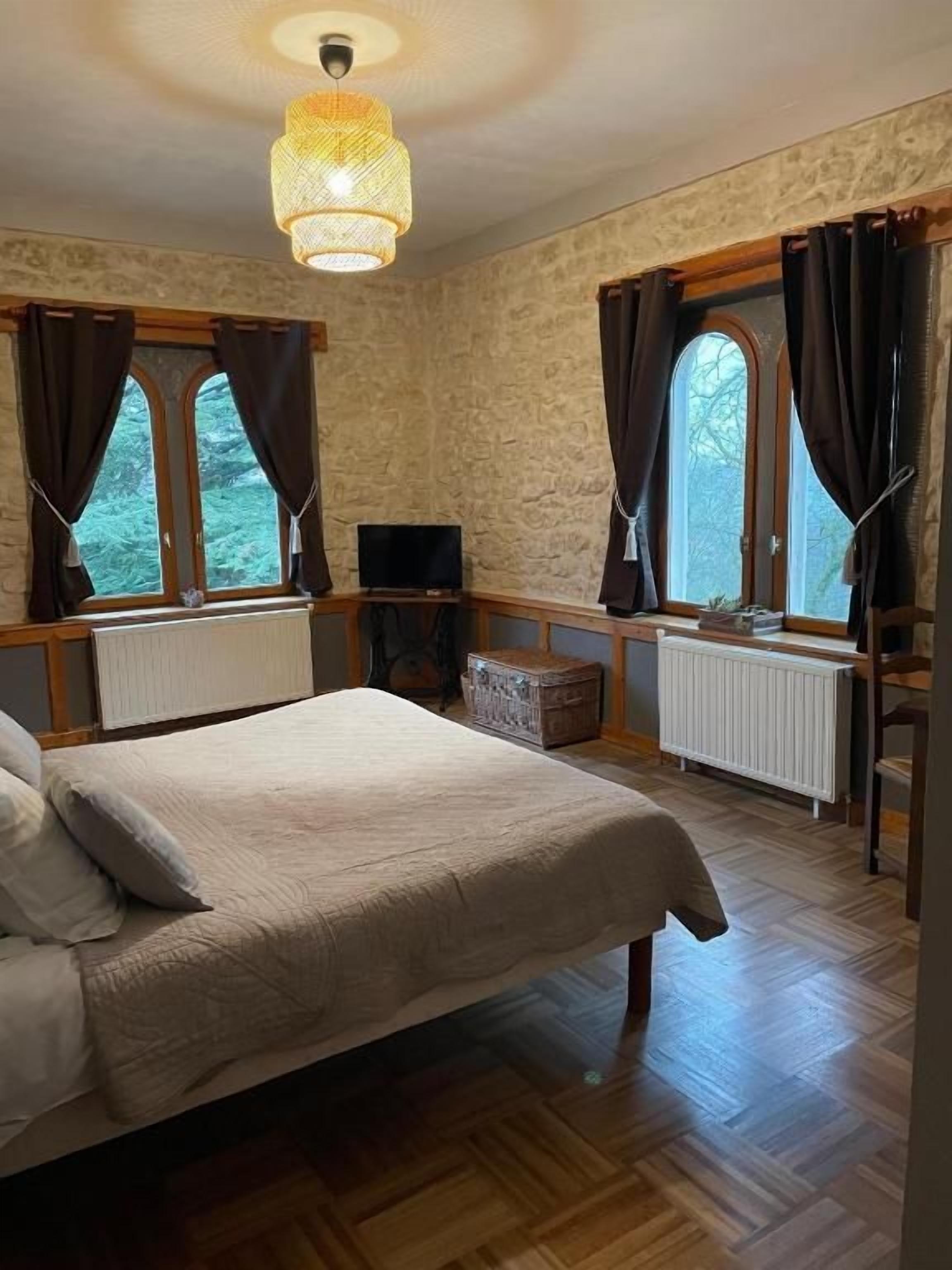 A bedroom with a bed, a television, a window with curtains, and a radiator.