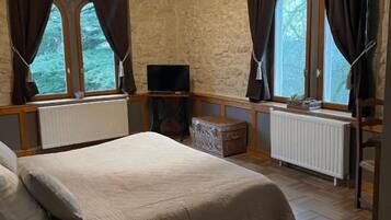 A bedroom with a bed, a television, a window with curtains, and a radiator.
