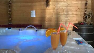Interior de una cabaña de madera con un jacuzzi, dos vasos de jugo de naranja con pajitas y un cuenco de galletas sobre una mesa.