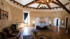 A spacious room with a large bed, wooden beams, stone walls, and a cozy fireplace.