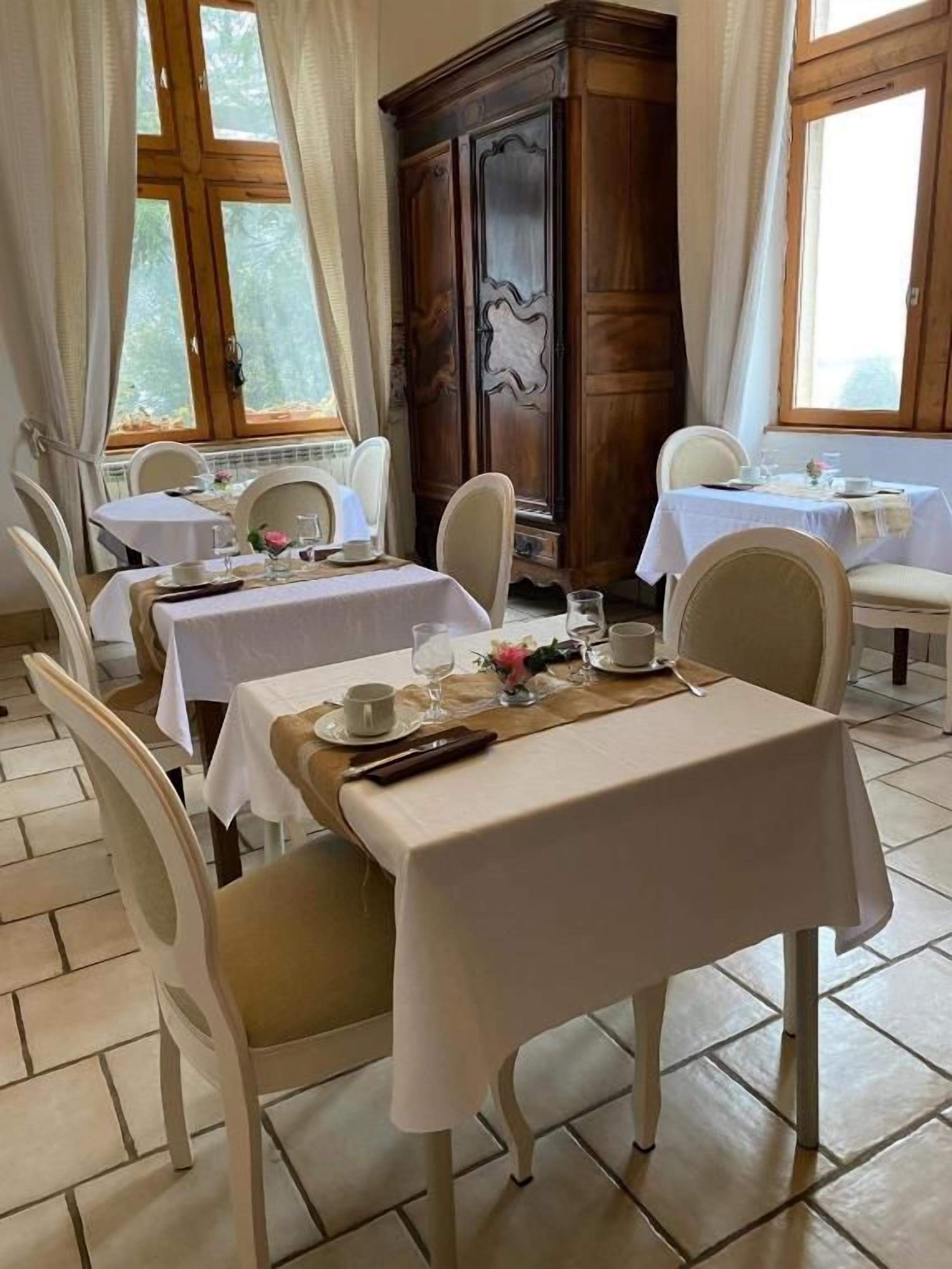 Un comedor con mesas dispuestas para dos, sillas blancas y un mueble de madera al fondo.