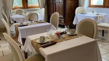 Un comedor con mesas dispuestas para dos, sillas blancas y un mueble de madera al fondo.