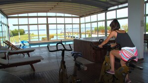 A covered outdoor area with a view of a lake, exercise bikes, and lounge chairs.