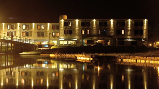 A multi-story hotel with a reflective pool in front, featuring a bridge and a well-lit facade.